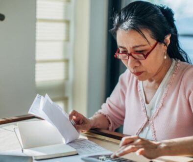 Woman in red glasses reviews papers about Medicare penalties at her desk, sunlight streaming through the window.