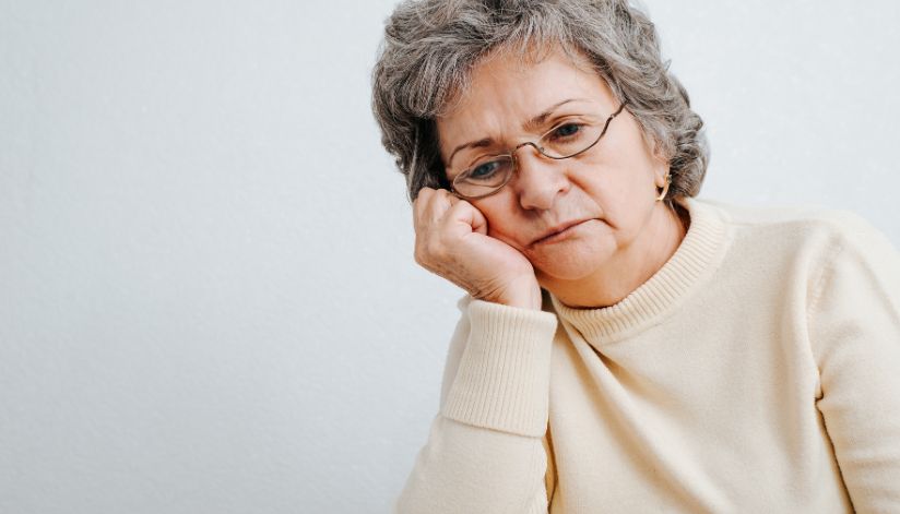 Older woman with short gray hair and glasses looks thoughtful, possibly reflecting on Medicare enrollment decisions.