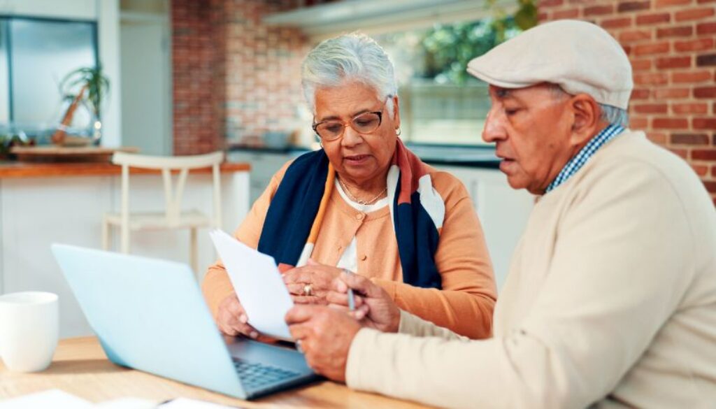 Two older adults review papers together at home, discussing Medicare Advantage options in front of a laptop.