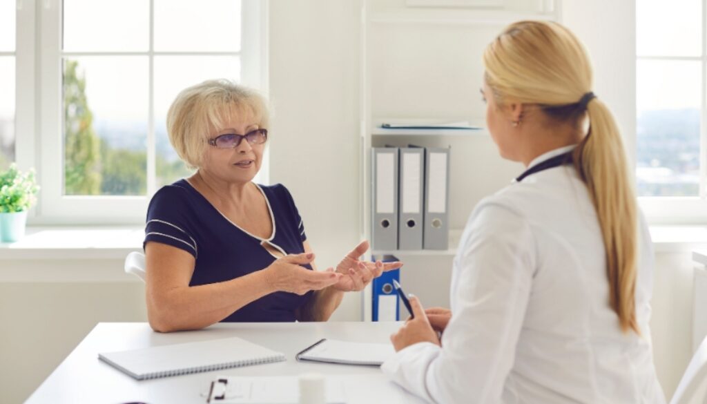 Older woman discusses GLP-1 Medicare coverage with a female doctor at a desk in a bright, organized office.